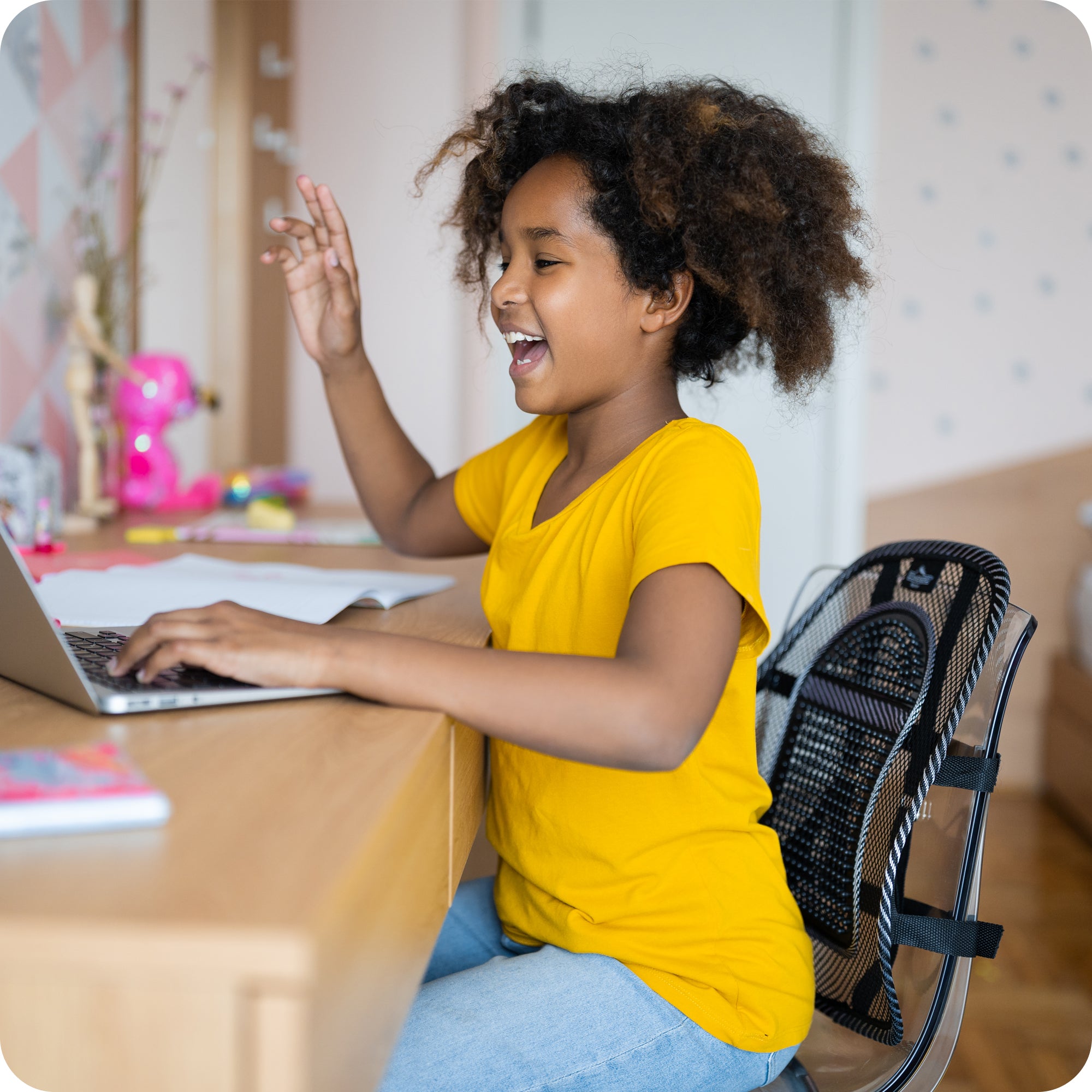 smiling young child at desk with ergonomic back support on her chair