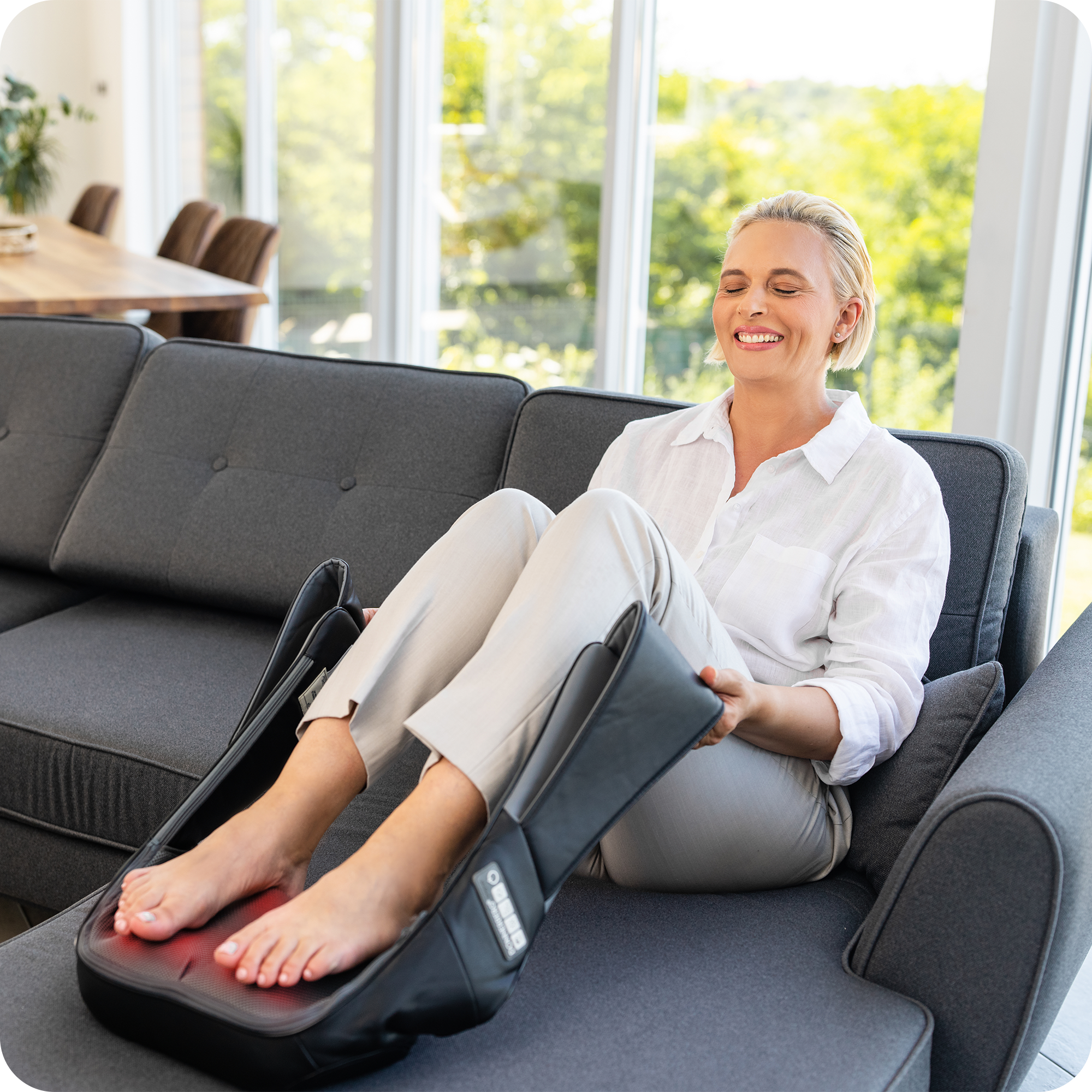 smiling woman enjoying foot massage while resting on bed