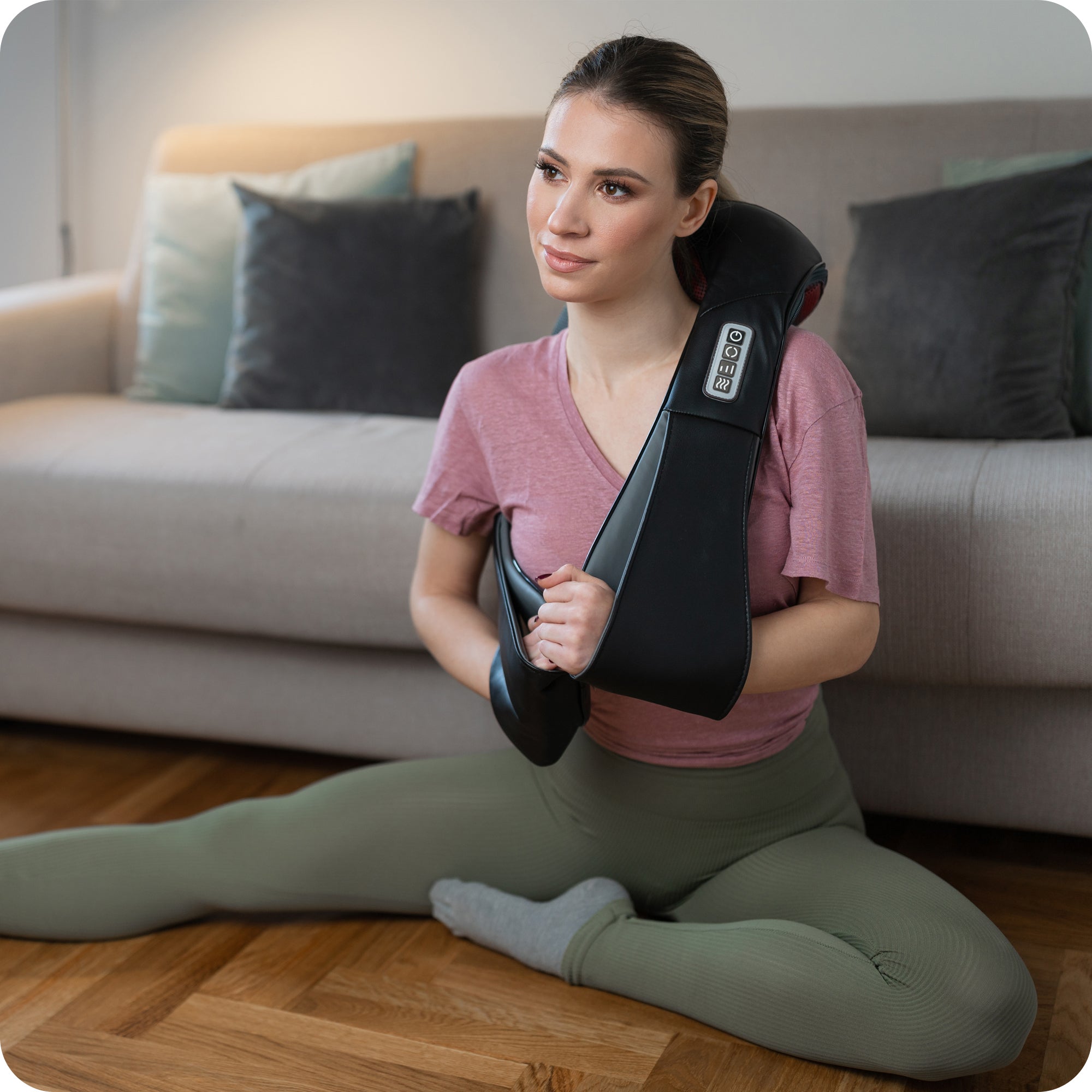 young woman using black electric massage machine in living room to relax sore shoulder muscles