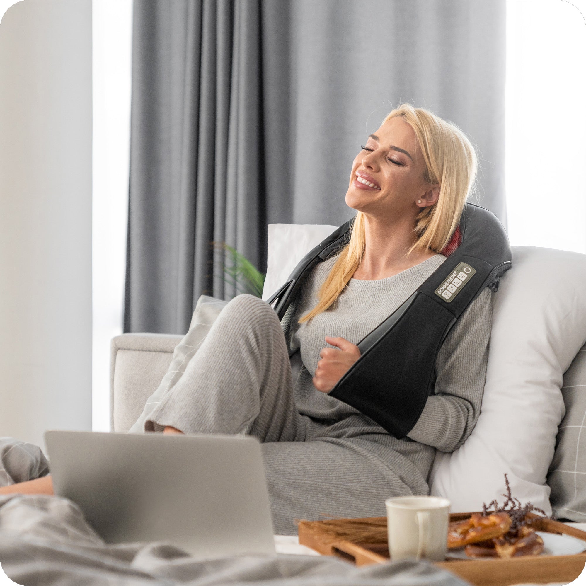 smiling woman using Donnerberg neck and shoulder massager while relaxing on bed