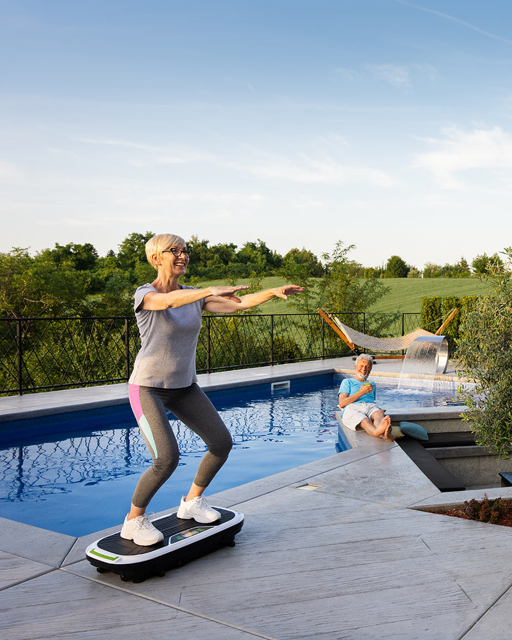 woman doing exercises on fitness vibration plate by the pool